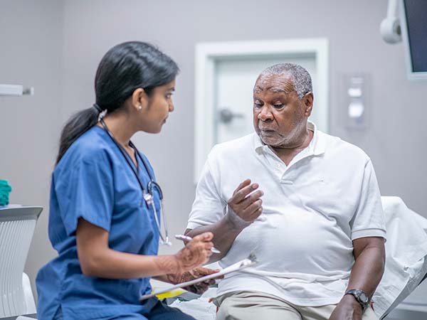 Older African American male patient sitting female doctor while the doctor takes notes