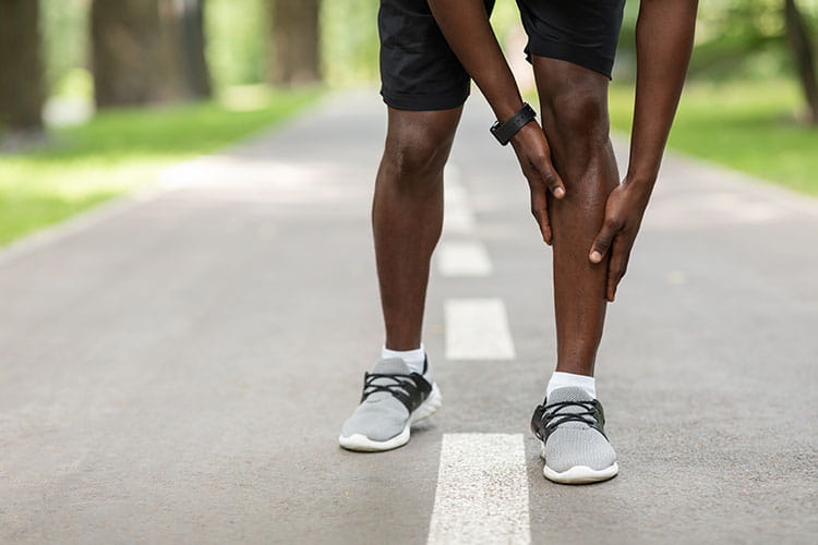 sportsman touching aching leg while jogging