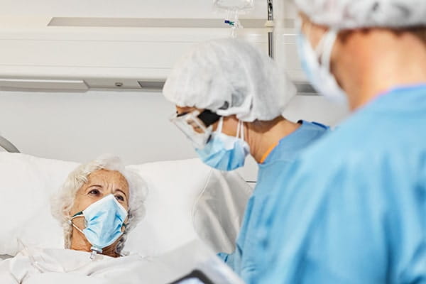Medical professionals examining elderly women in patient in ICU lying in bed.
