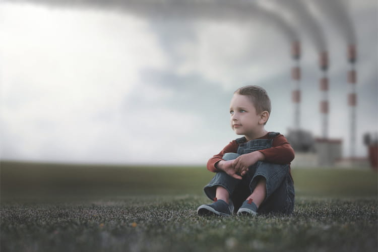 boy sitting on grass with smokestacks in the background